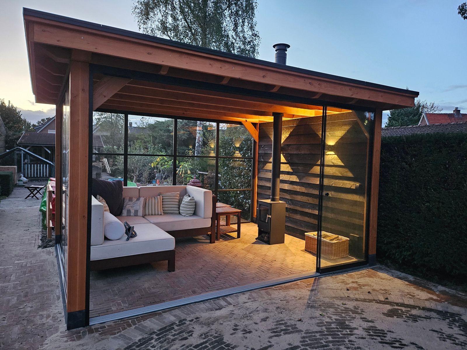 Houten overkapping met loungeset en houtkachel in de avond