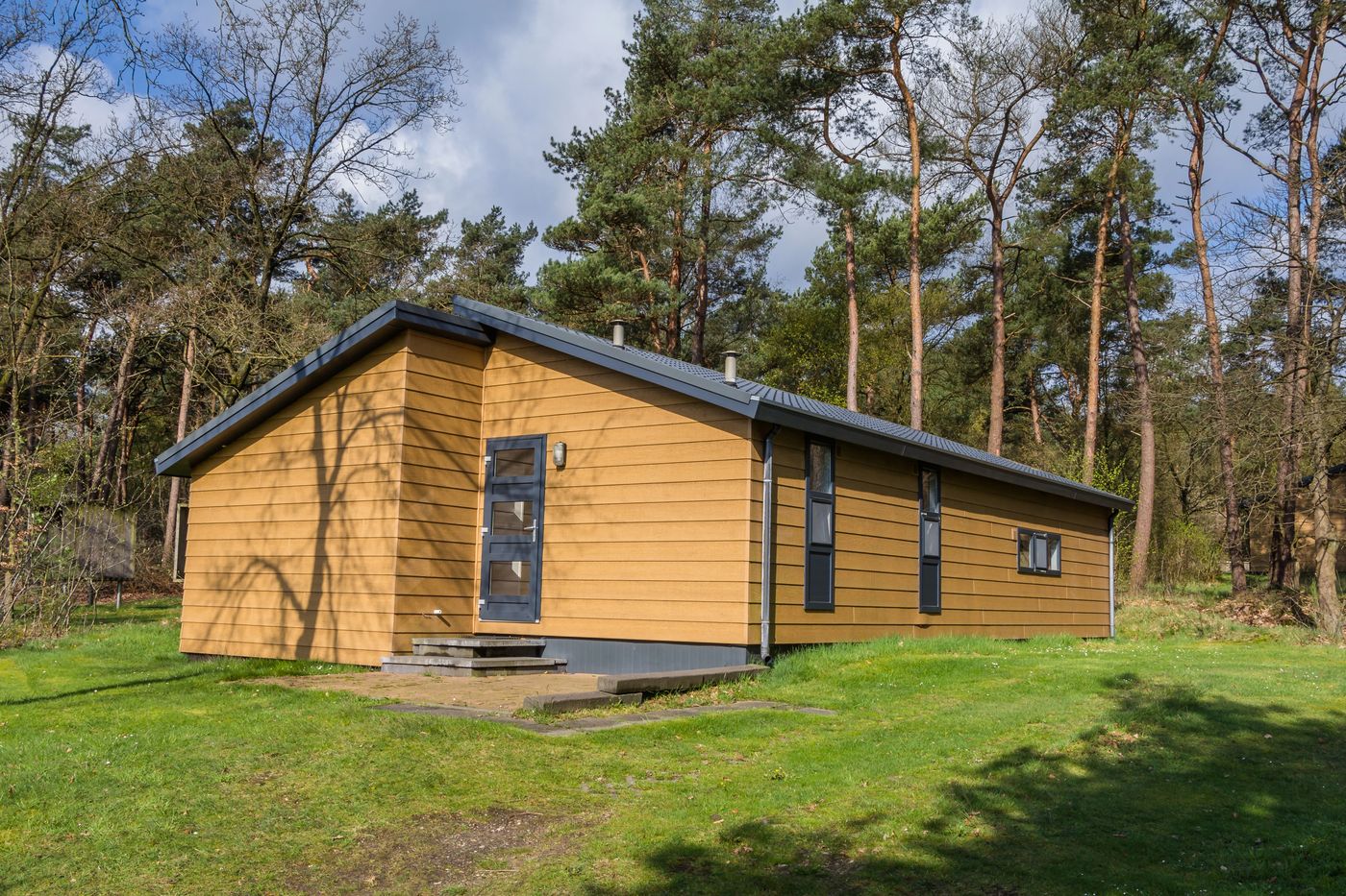 Recreatiewoning met houten gevel tussen dennenbomen